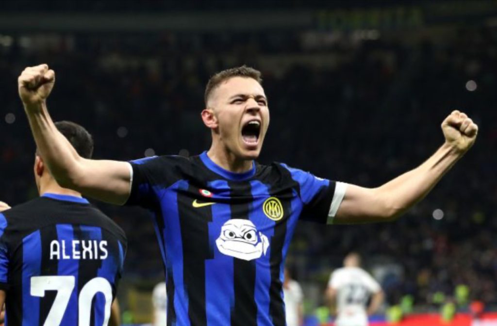 A male football player, possibly Inter Milan's Nicolò Barella, in a blue and black striped jersey (featuring the U-Power sponsor logo), celebrates exuberantly on a brightly lit football pitch